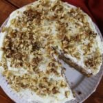 The top of a cake with a slice taken out of it with white frosting and chopped walnuts on it.