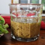 glass jar with tangy mustard salad dressing in it sitting on a table.