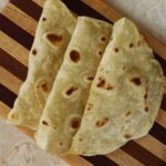 Three folded homemade tortilla shells on a striped cutting board.