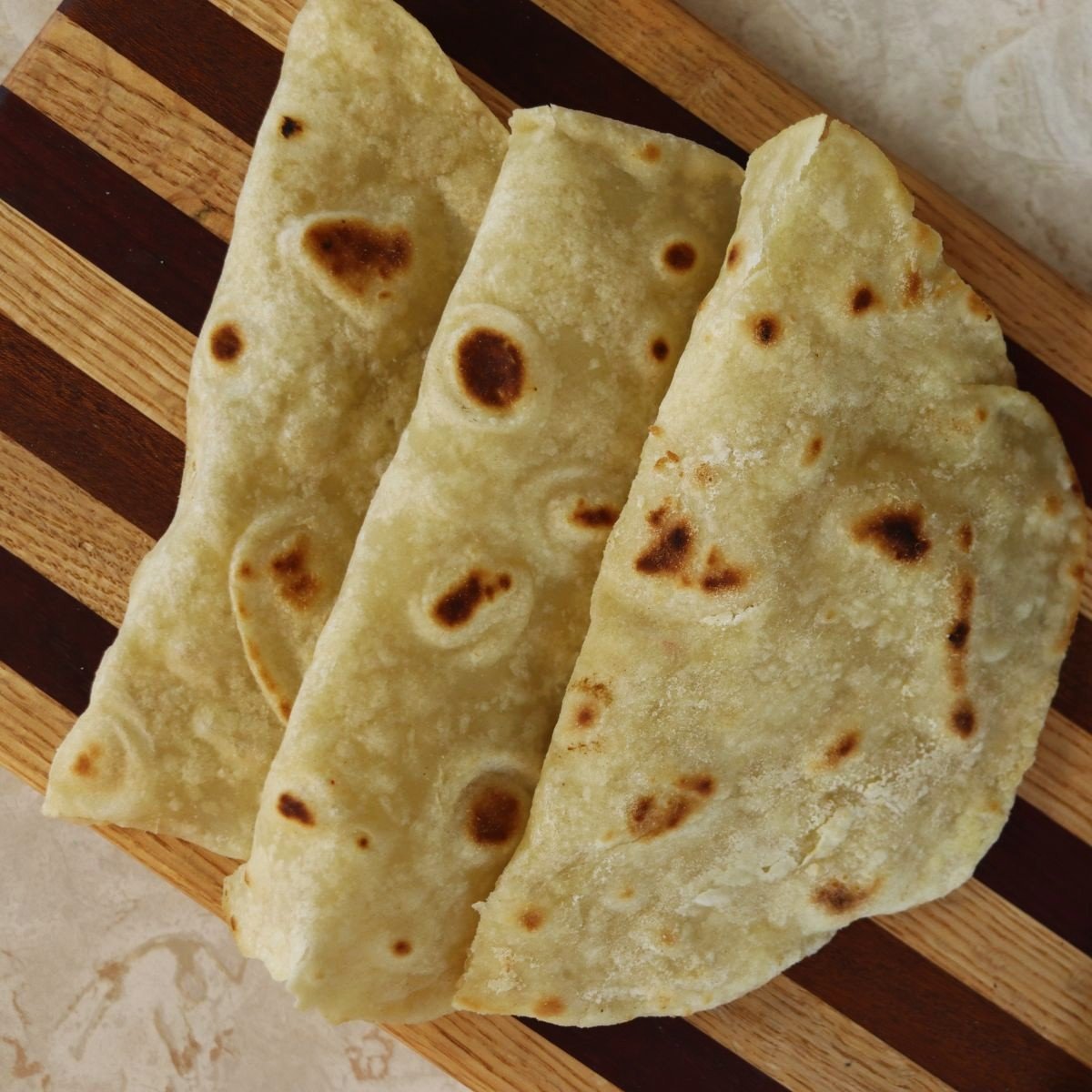 overview of three homemade tortilla shells folded and lined up on a cutting board.