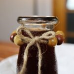 The top of a glass jug full of red liquid with jute twine and wooden beads around the bottleneck.
