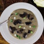 Creamy soup topped with mushroom and scallion slices in a white bowl with a spoon in it.
