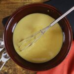 a bowl of vegan honey mustard with a whisk in the bowl and measuring spoons on the side.