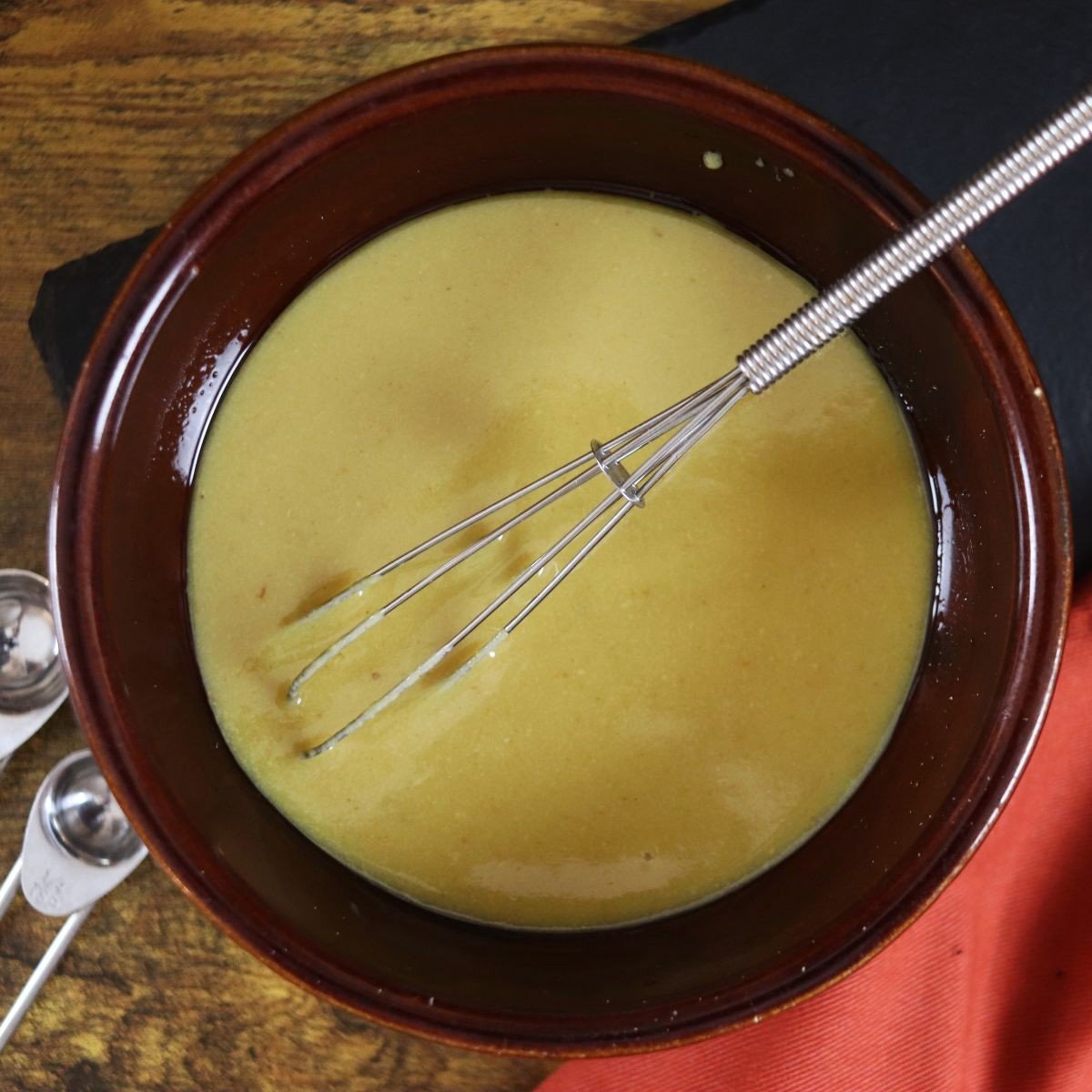 a bowl of vegan honey mustard with a whisk in the bowl and measuring spoons on the side.