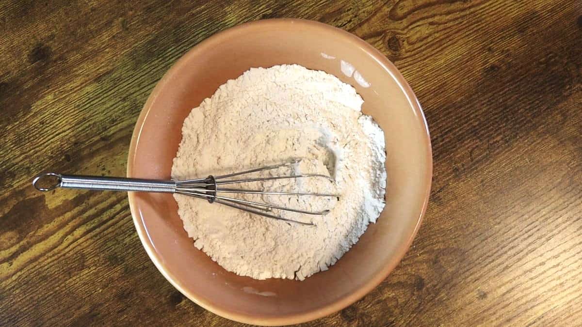 Flour mixture in a bowl with a whisk sitting on a wooden surface.