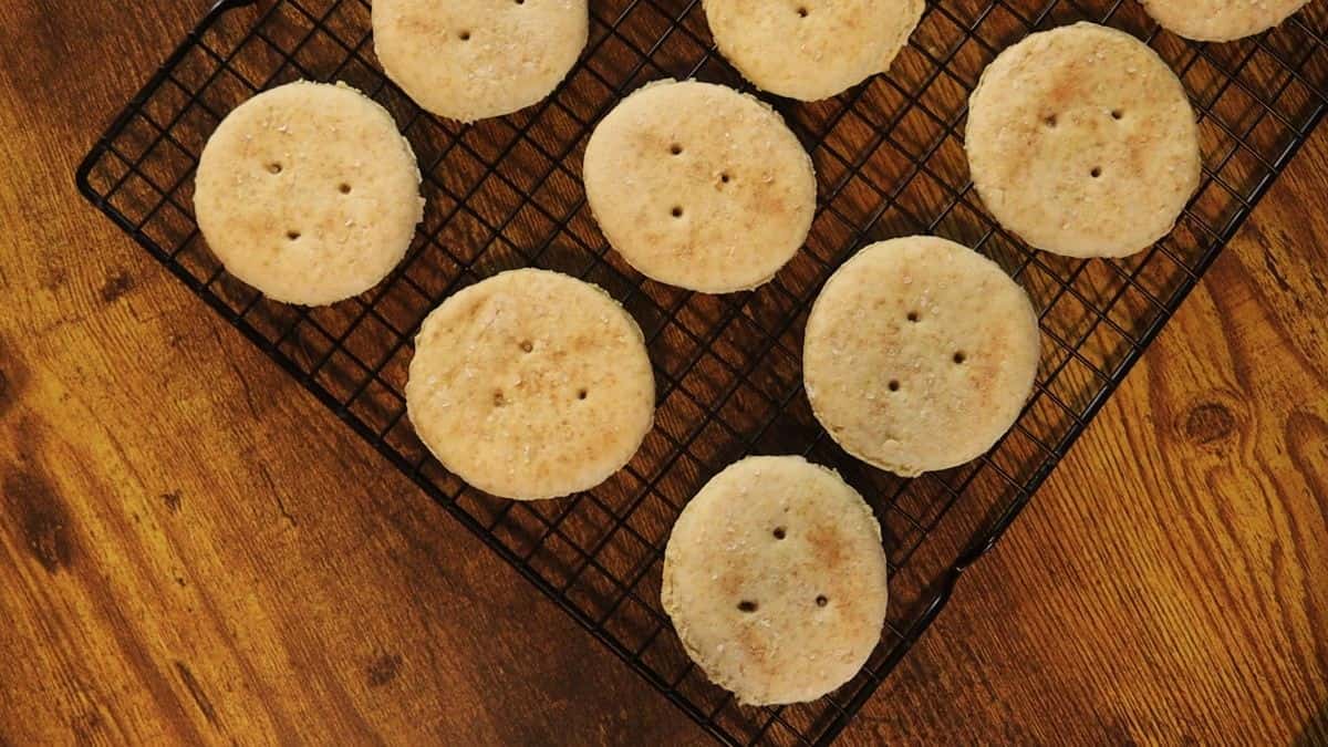 Golden, round baked crackers sitting on a wire cooling rack on a wooden table.