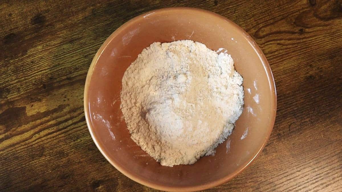 Flour mixture with a light crumb texture in a bowl on a wooden surface.