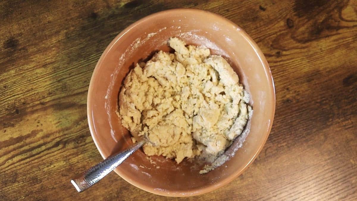 Shaggy dough in a bowl with a fork in it on a wooden surface.