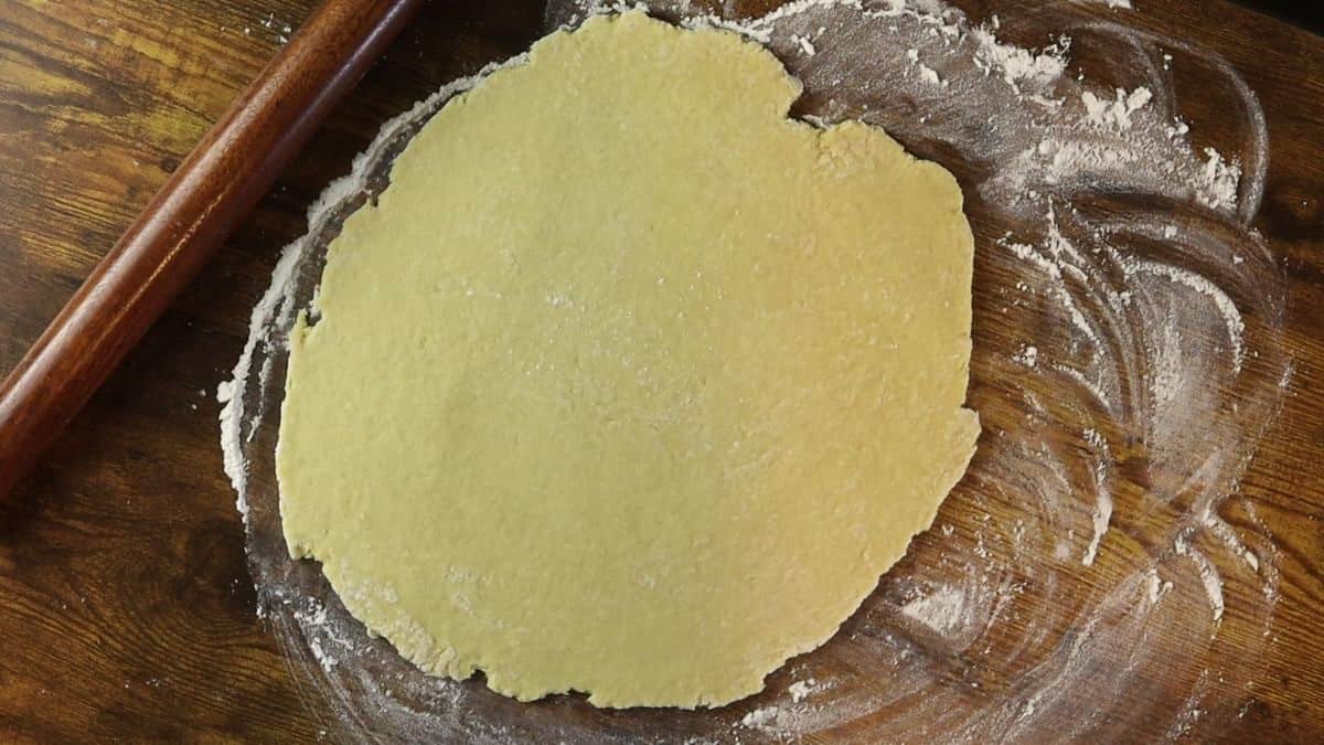 yellow dough rolled out on a floured wooden surface.