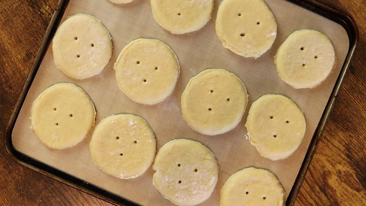 Rounds of dough with 3 puncture holes in them laid out on a tan silicone mat.