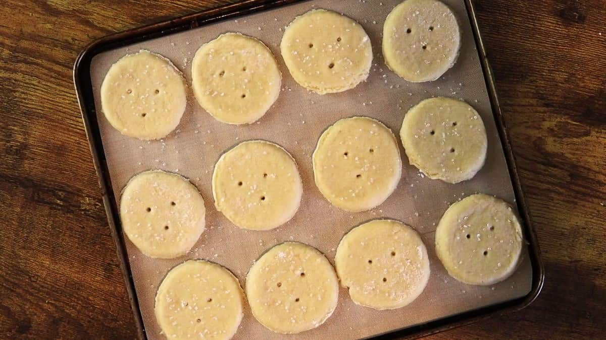 Rounds of dough with holes punctured in them topped with coarse salt on a tan silicone mat.