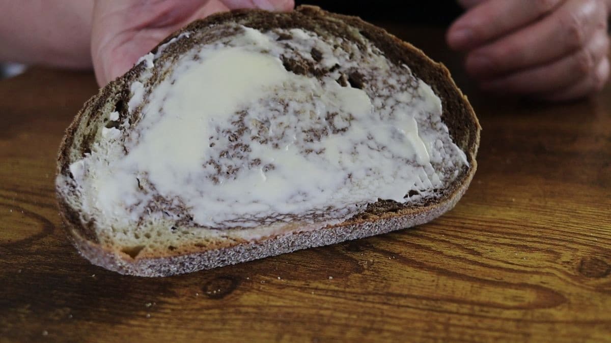 Hands holding a slice of buttered marbled rye bread over a wooden surface.