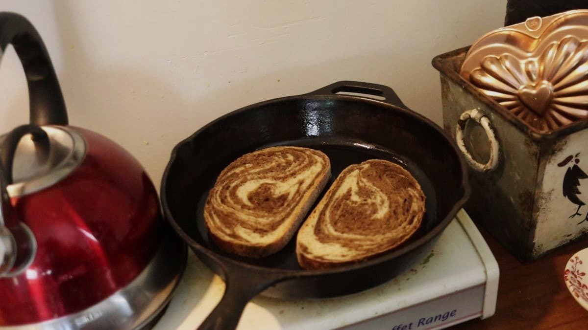 Two slices of rye bread in a cast iron skillet on a small stovetop.