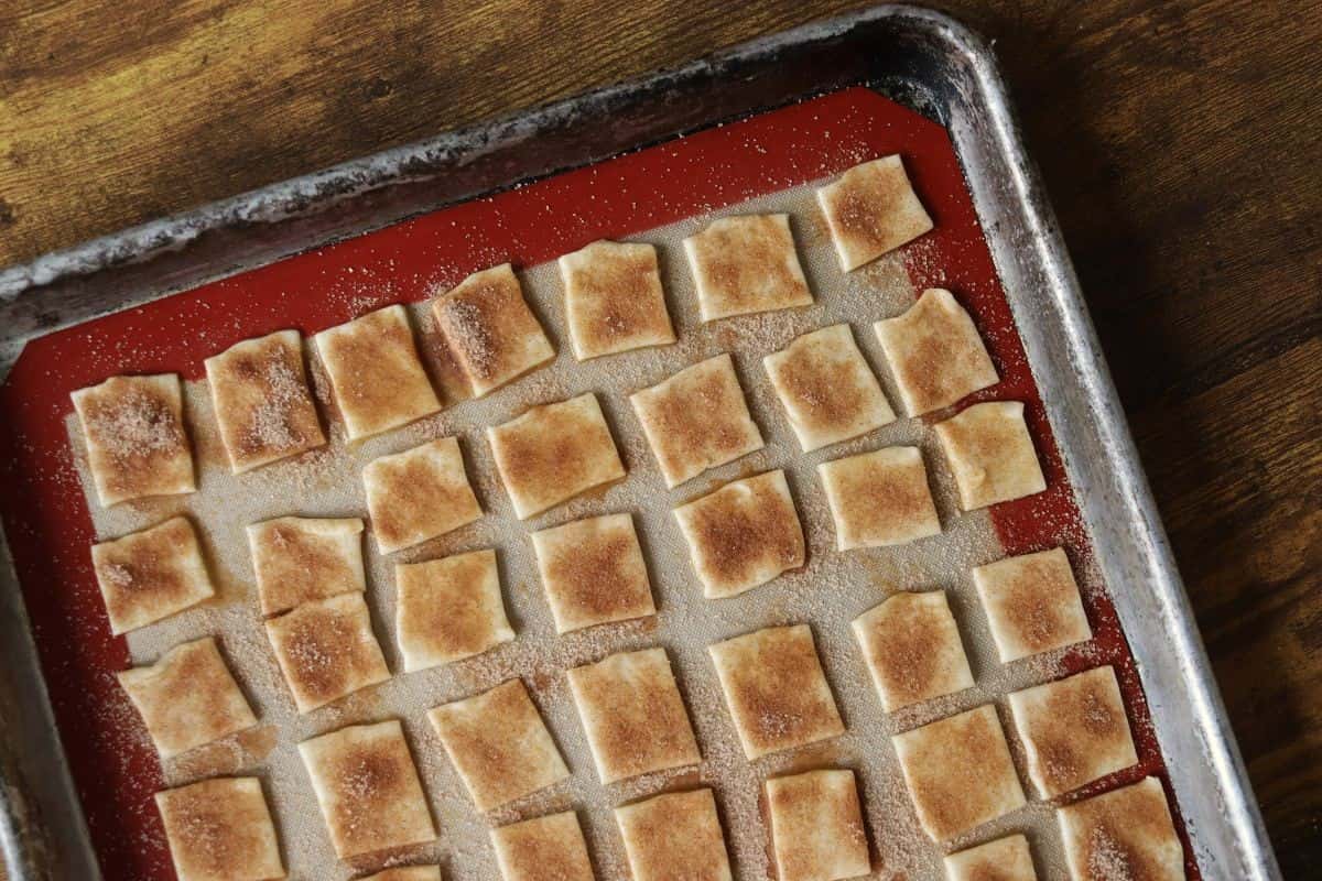 Unbaked square crackers with a cinnamon sugar topping on them on a silicone lined baking sheet.
