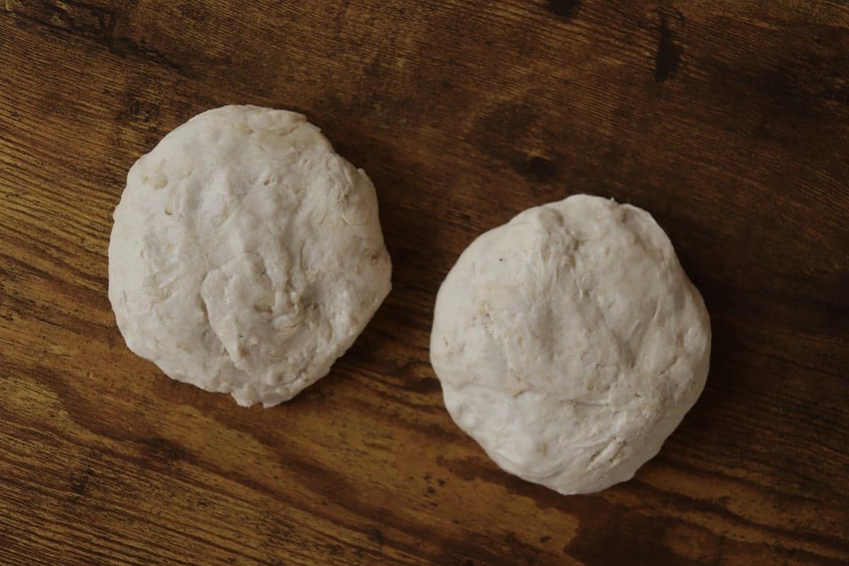 Two dough balls sitting next to each other on a wooden surface.