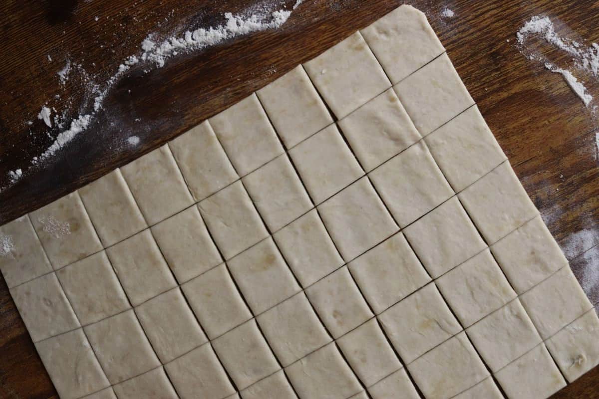 Rolled out dough cut into squares on a floured wooden surface.