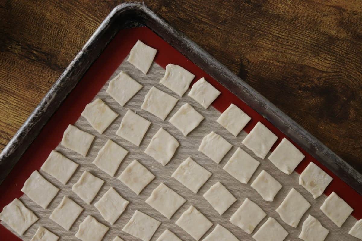 Unbaked square crackers sitting on a silicone lined baking sheet.