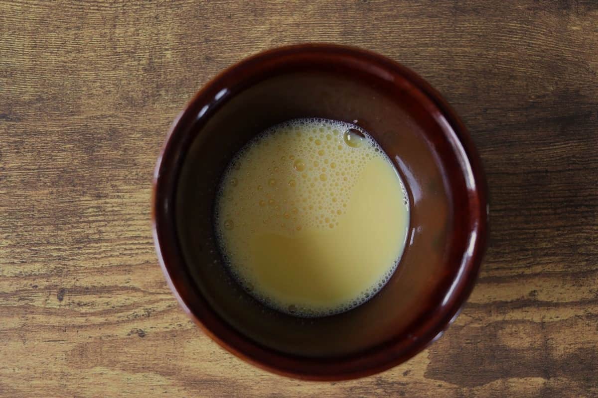 Beaten egg in a brown bowl sitting on a wooden surface.
