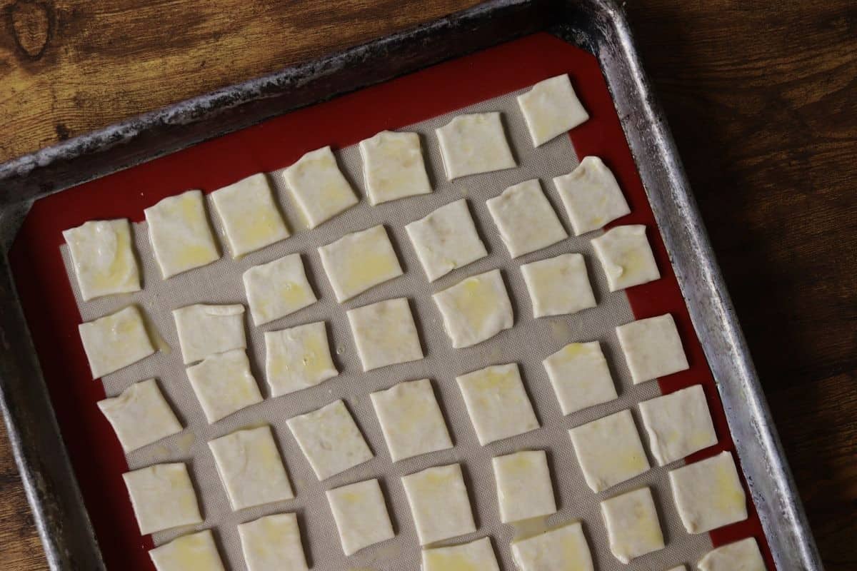 Unbaked square crackers with egg brushed on them sitting on a silicone lined baking sheet.