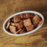 White oval dish full of brown cinnamon sugar coated crackers sitting on a wooden surface.