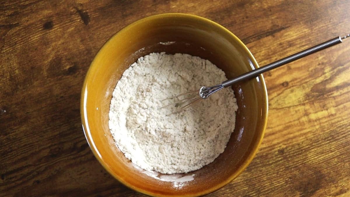 Flour mixture in a brown bowl with a whisk in it sitting on a wooden surface.