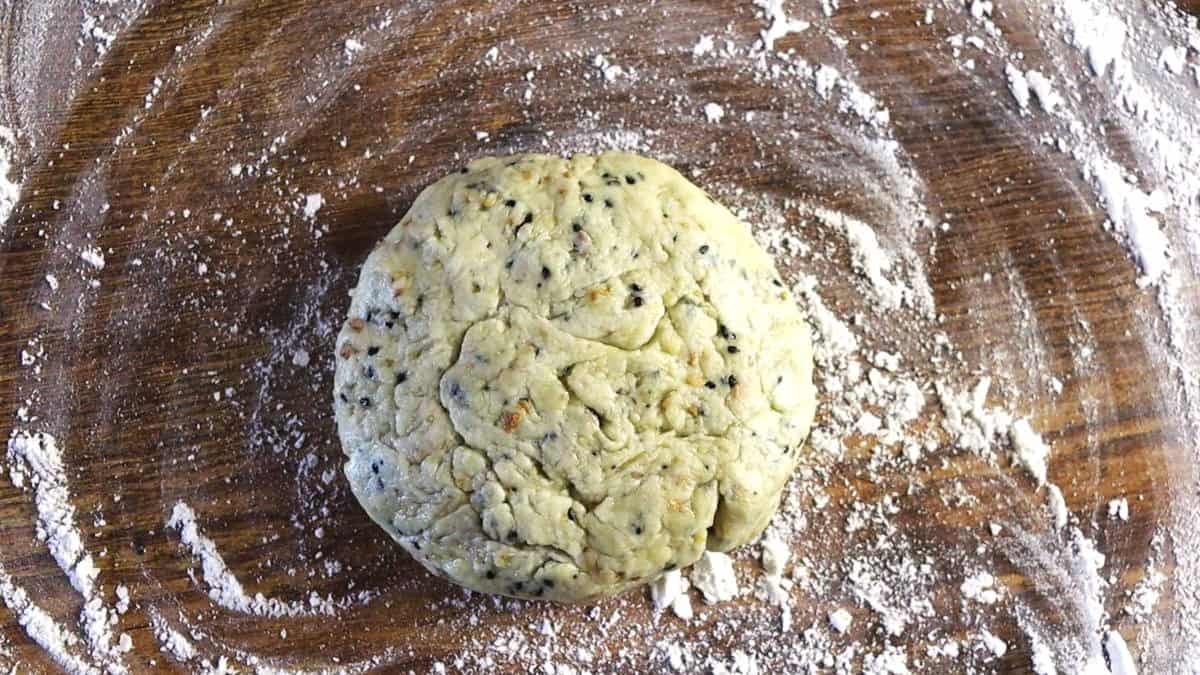 Disk of dough with seeds visible in it sitting on a floured wooden surface.