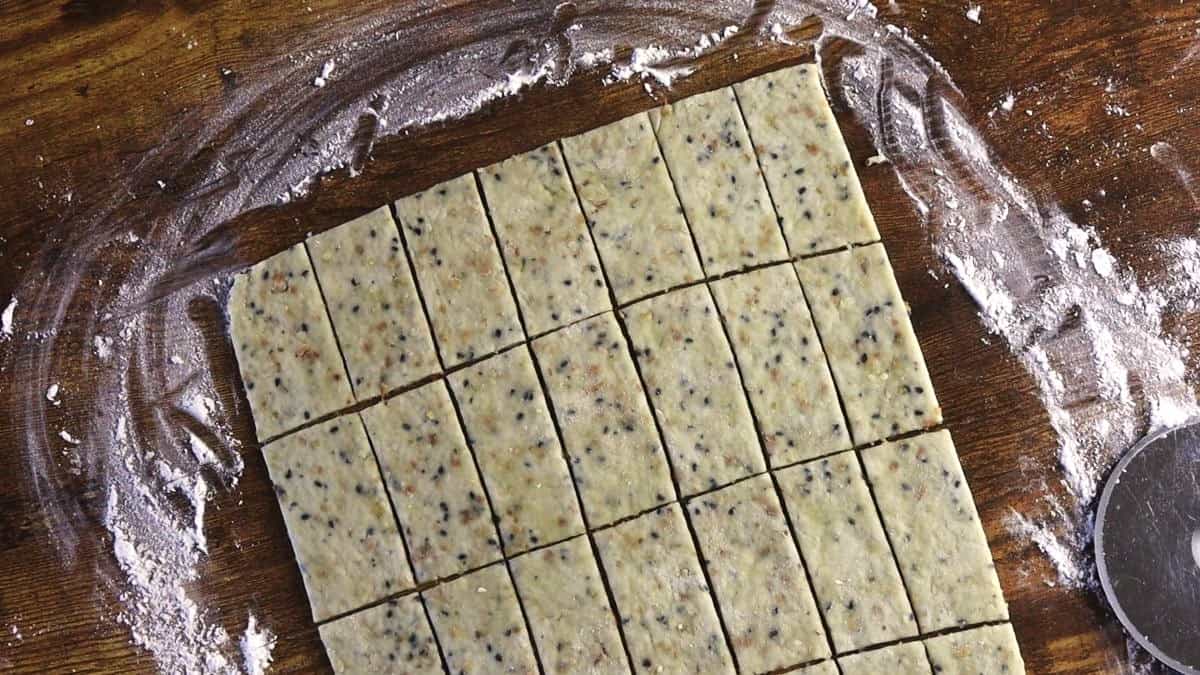 Dough with seeds visible in it cut into rectangular shapes on a floured wooden surface.