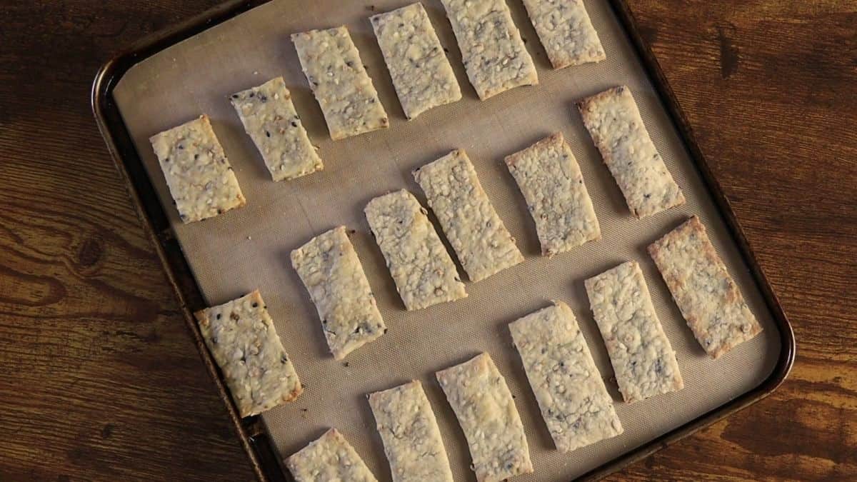 Baked rectangular crackers with seeds visible in them sitting on a silicone lined baking sheet.