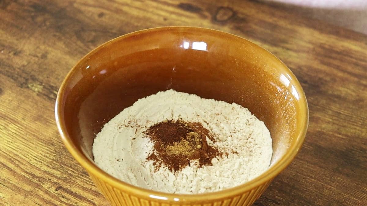 Flour with brown spices on top in a bowl on a wooden surface.