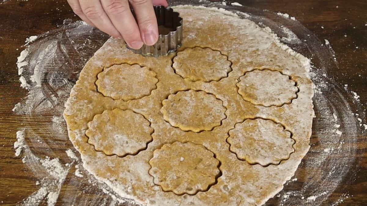 Hand using a cookie cutter cutting round shapes with scalloped edges out of orange dough.