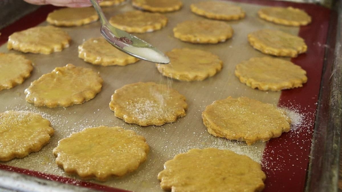 Spoon sprinkling sugar over raw orange crackers on a baking sheet.