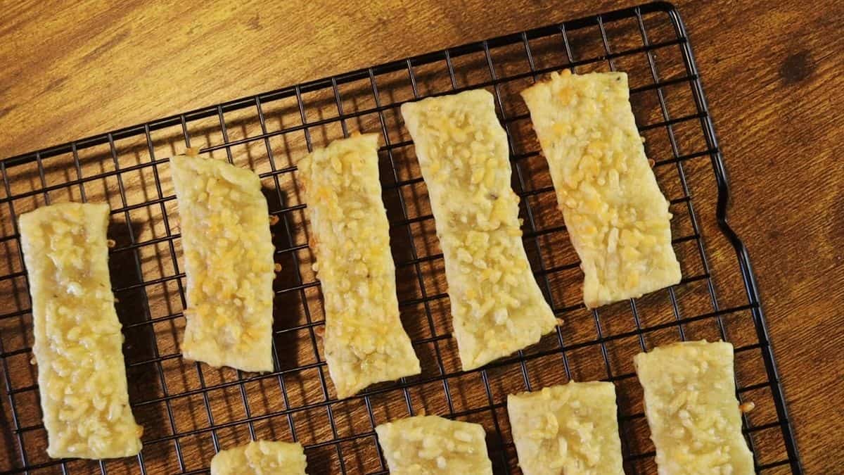 Rectangular crackers topped with cheese sitting on a cooling rack.