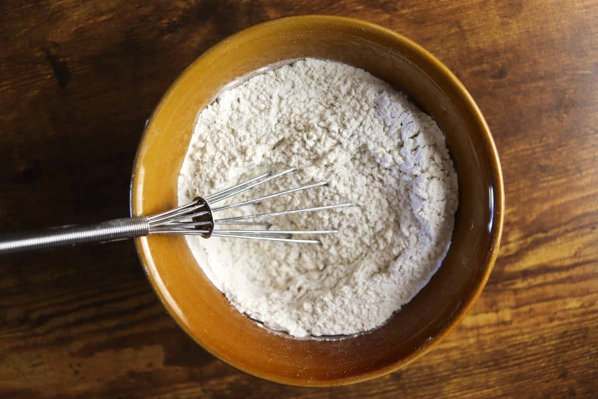 Flour mixture in a bowl with a whisk in it sitting on a wooden surface.