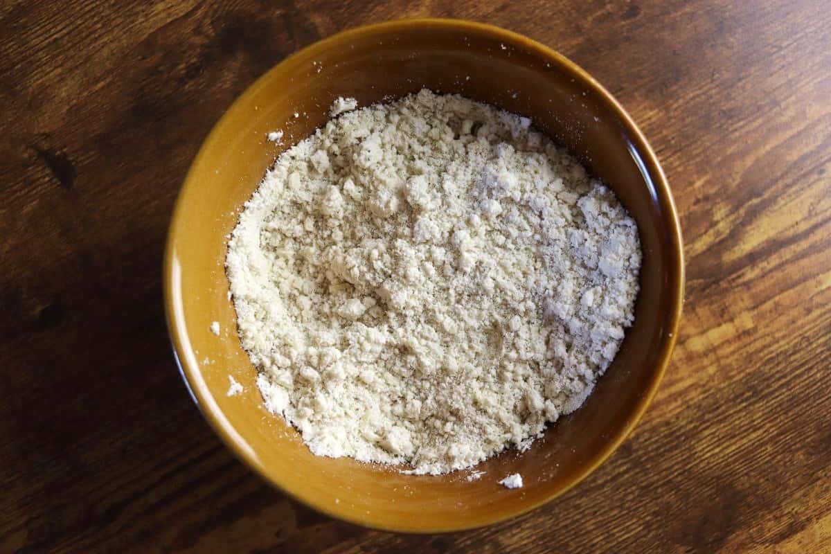 Flour mixture with the texture of coarse sand in a bowl sitting on a wooden surface.