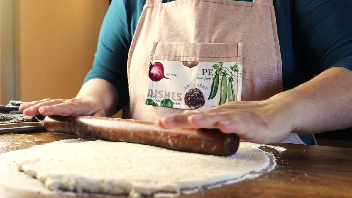 Woman rolling out dough on a floured surface.