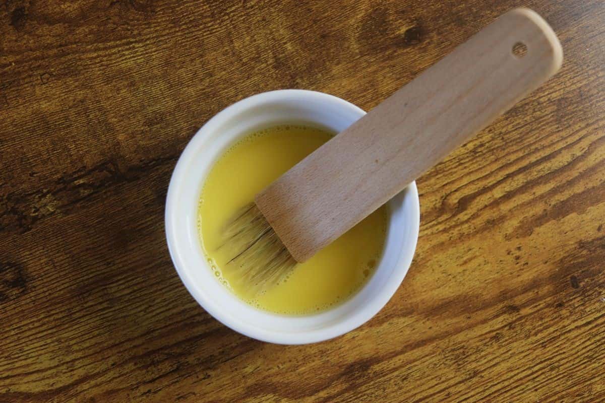 Beaten egg mixture in a small white bowl with a basting brush in it.