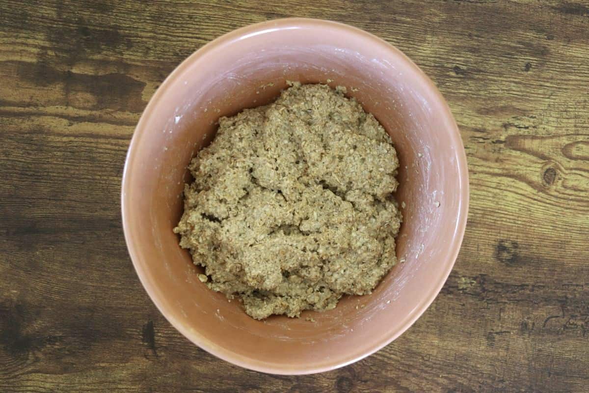 Grainy dough in a bowl sitting on a wooden surface.