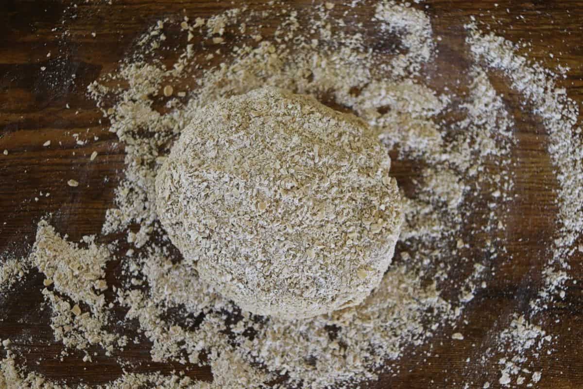 Round ball of dough covered in grainy flour sitting on a flour covered surface.