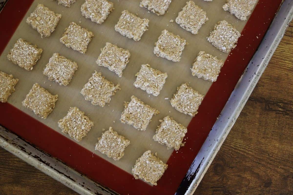 Square grainy dog treats sitting on a silicone lined baking sheet.