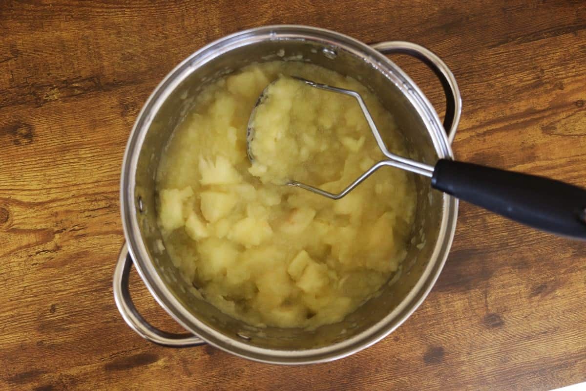 Partially mashed, cooked apple chunks in a pot on a wooden surface.