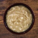 Homemade applesauce with a chunky texture in a brown bowl sitting on a wooden surface.