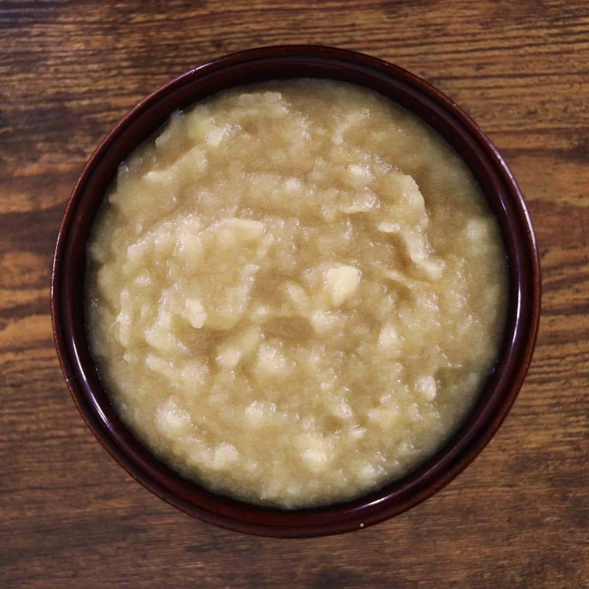 Homemade applesauce with a chunky texture in a brown bowl sitting on a wooden surface.