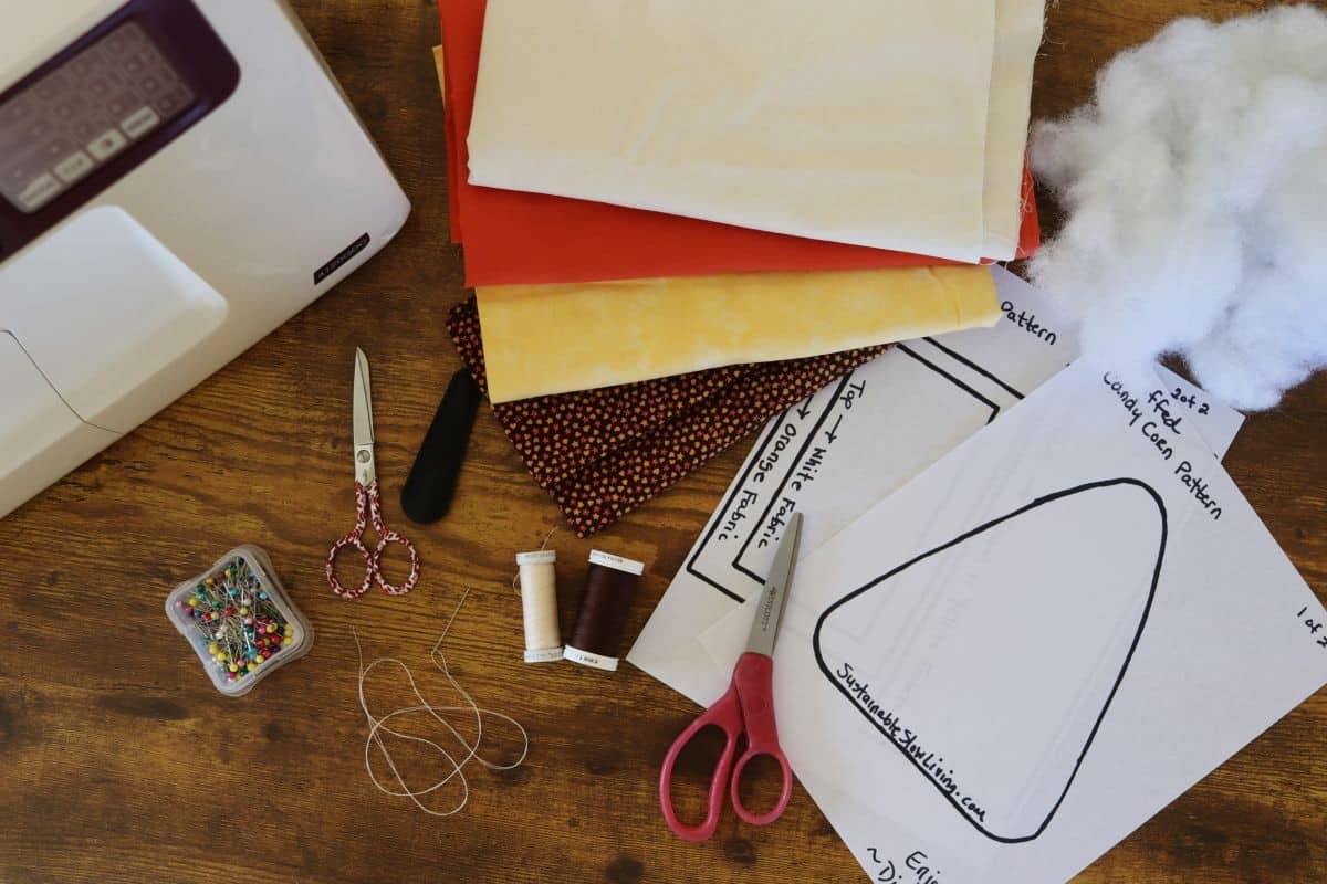 A sewing machine, fabric pieces, scissors, pins, thread, stuffing, and printed pattern templates are arranged on a wooden table, ready for a sewing project.