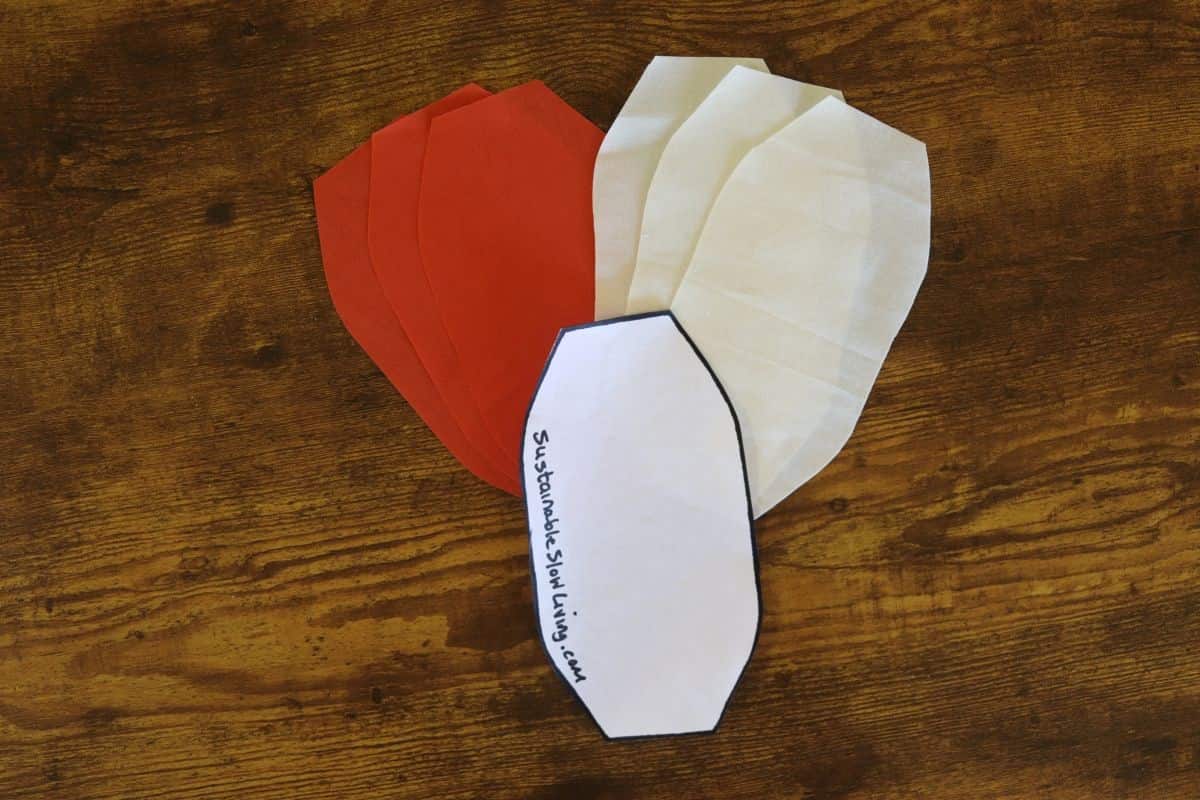 6 oval fabric pieces, 3 orange and 3 white, on a wooden surface with an oval paper pattern piece.