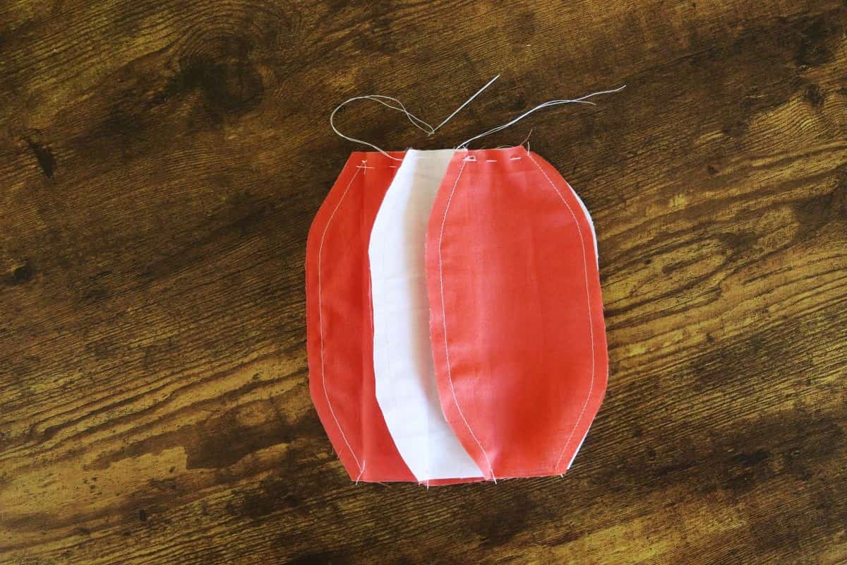 White and orange oval shaped fabric panels sewn together in a circle with a basting stich along the top edge.