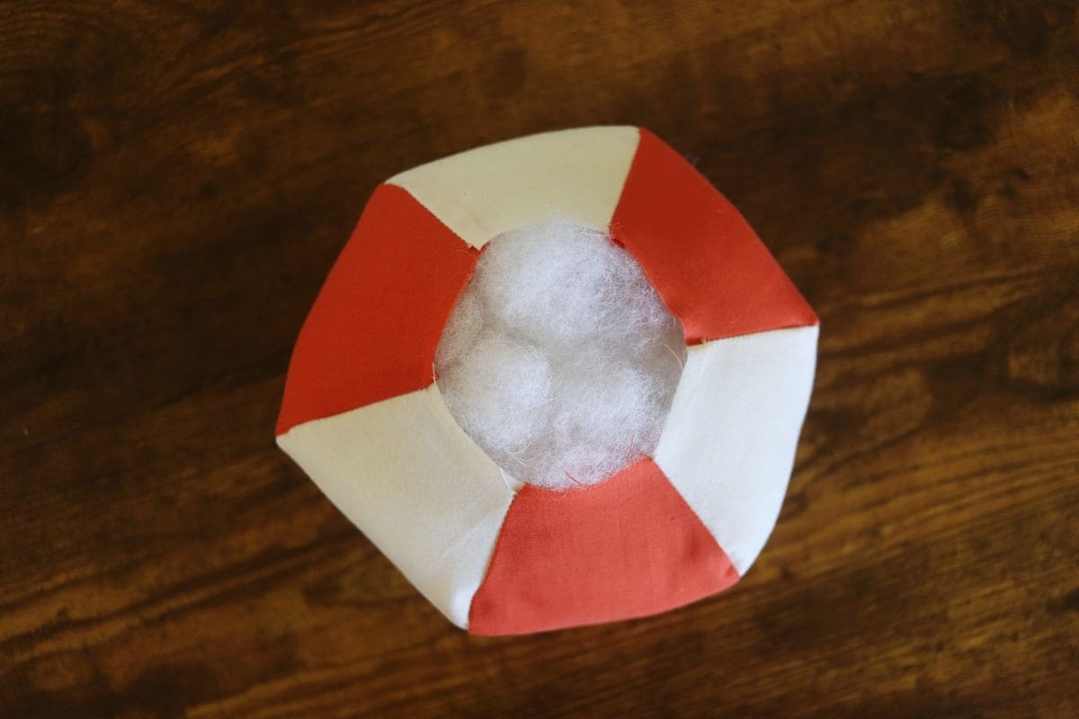 White and Orange fabric panels sewn together to create a ball shape with the one end open showing the stuffing inside. 