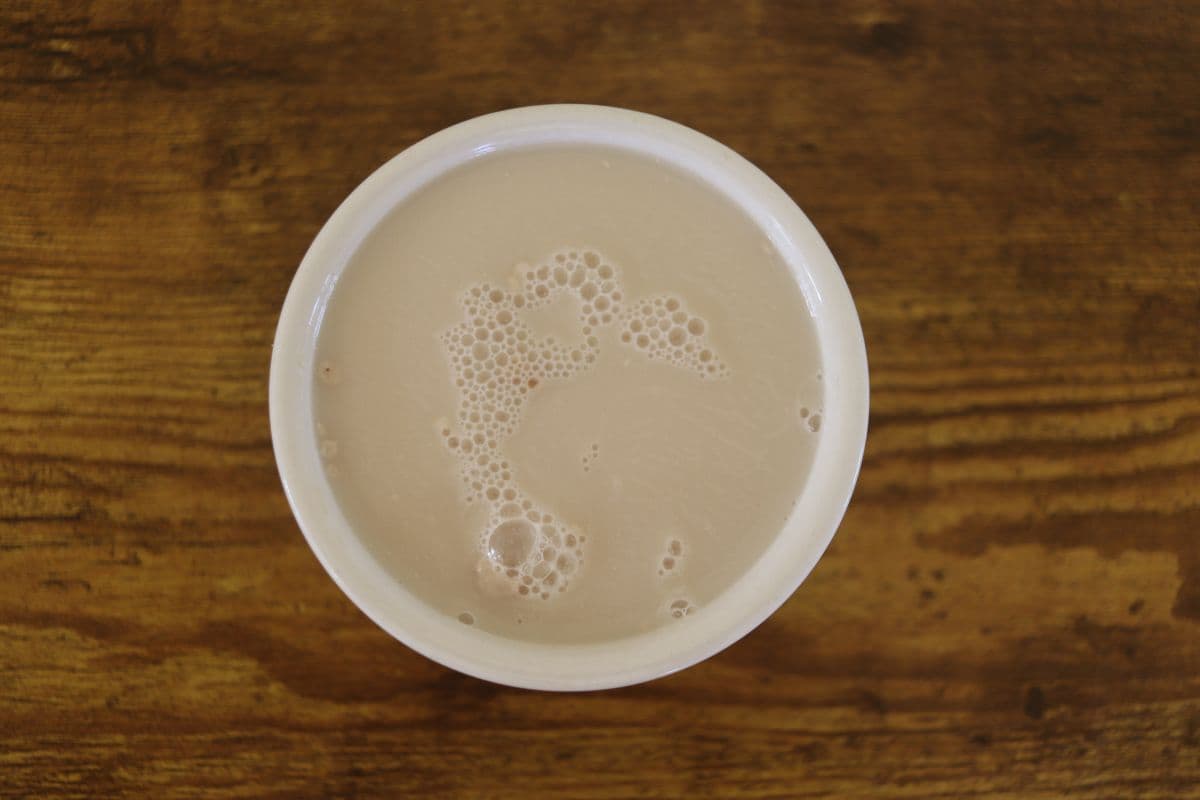 Creamy colored liquid in a white bowl on a wooden surface.