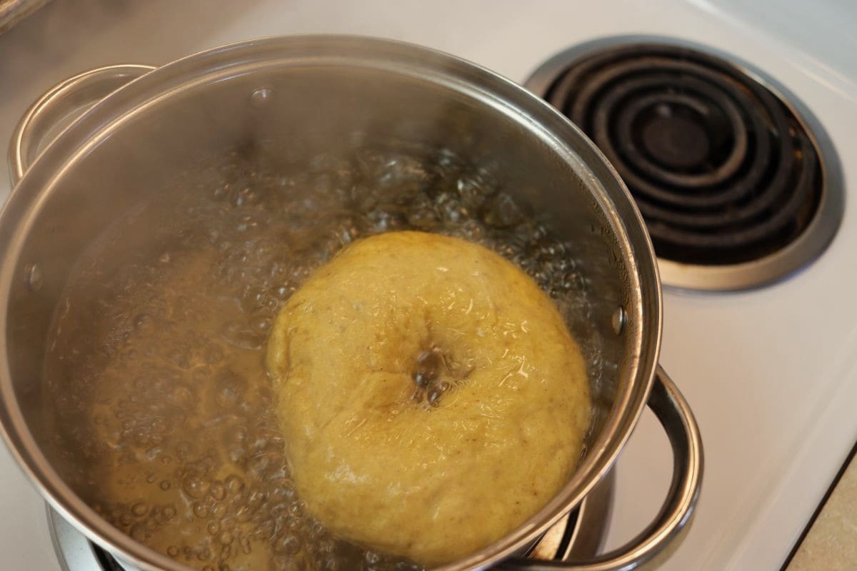 Orange colored bagel in a pot of boiling water on a stovetop.