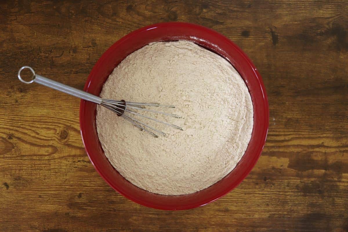 Flour mixture with a whisk in it in a red bowl sitting on a wooden surface.