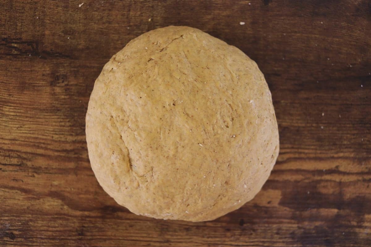Ball of orange colored dough sitting on a wooden surface.
